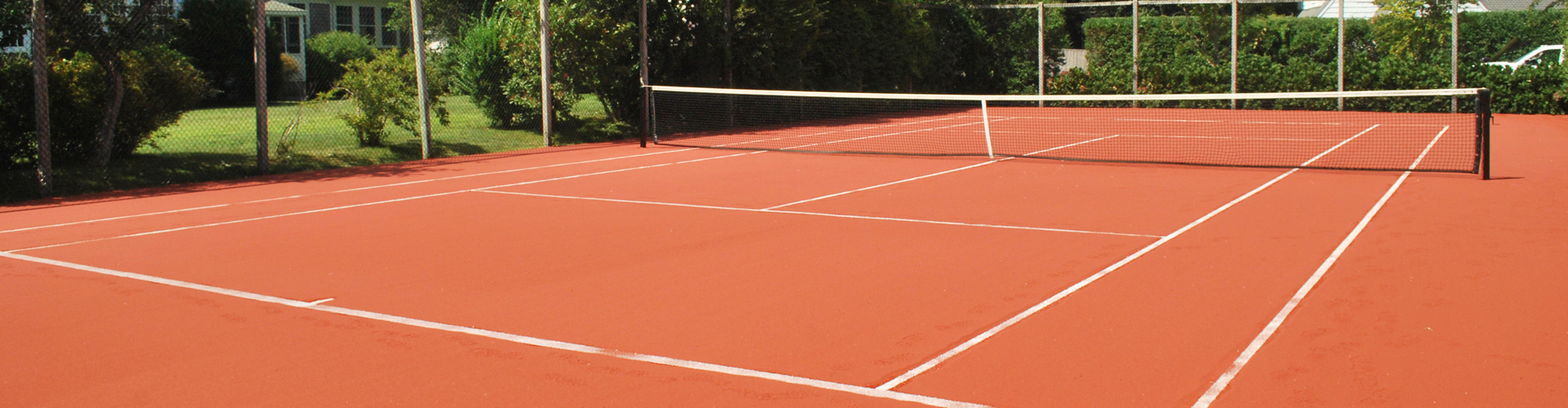 Residential clay-style tennis court with net and surrounding landscaping installed by Southwest Greens